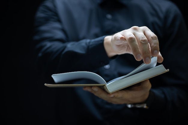 Ein Mann im schwarzen Gewand hält ein Buch vor sich und versucht die Seite umzublättern