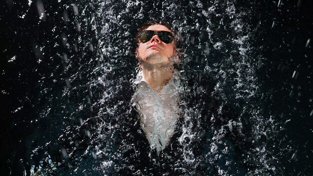 Ein Mann in Anzug und Sonnenbrille taucht im Regen ins Wasser