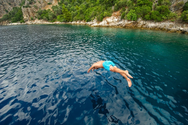 Ein Mann in blauen Shorts taucht von einem Schiff ins Meer nahe der Küste