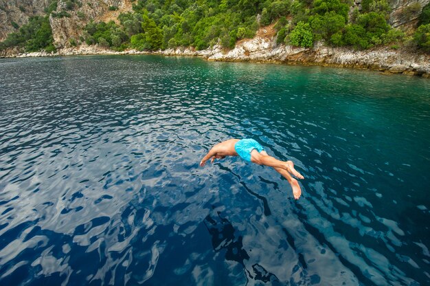 Ein mann in blauen shorts taucht von einem schiff ins meer nahe der küste