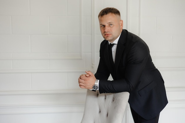 ein Mann in einem Anzug und einer Uhr steht vor einer weißen Wand