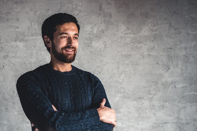 Ein Mann in einem blauen Pullover auf einem grauen Hintergrund.