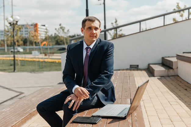 Ein Mann in einem Business-Anzug und einem Laptop sitzt auf einer Bank. Geschäftsmann mit Laptop.