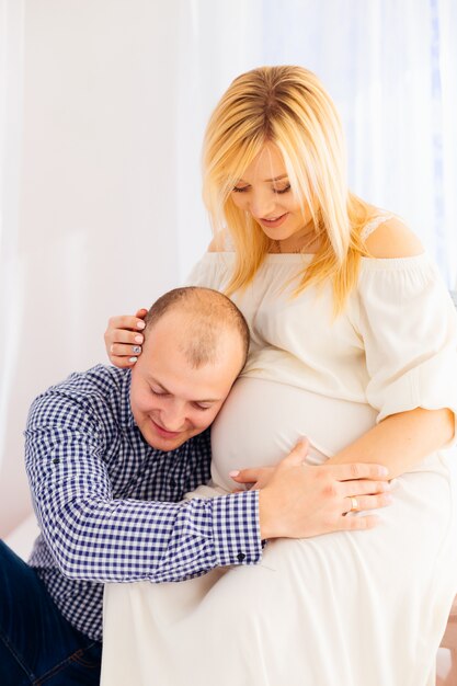 Ein Mann in einem eleganten Hemd sitzt neben seiner schwangeren Frau