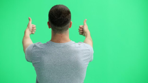 Foto ein mann in einem grauen t-shirt auf einem grünen hintergrund zeigt seine daumen nach oben