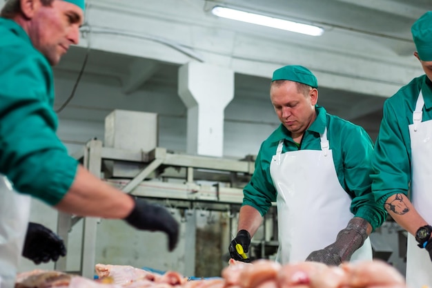 Ein Mann in einem grünen Kittel schneidet Fleisch in einer Fabrik.