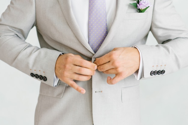 Ein Mann in einem hellgrauen Anzug mit lila Krawatte knöpft ihn zu.