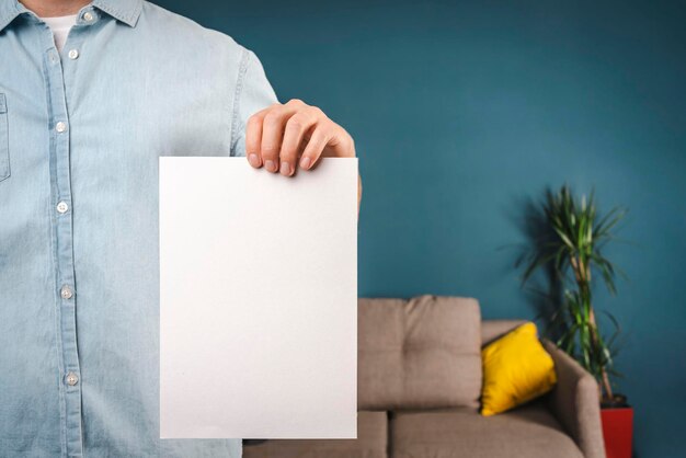 Ein Mann in einem Hemd hält zu Hause ein weißes Blatt Papier in der Hand