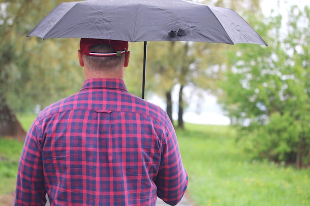 Ein Mann in einem karierten Hemd unter einem schwarzen Regenschirm im Park