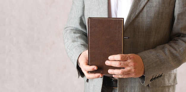 Ein Mann in einem klassischen Kostüm hält ein braunes Buch. Nahansicht