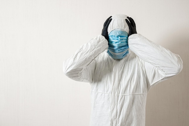 Foto ein mann in einem schutzanzug mit medizinischen masken, der vor einem wandhintergrund posiert und verschiedene gesten mit den fingern zeigt