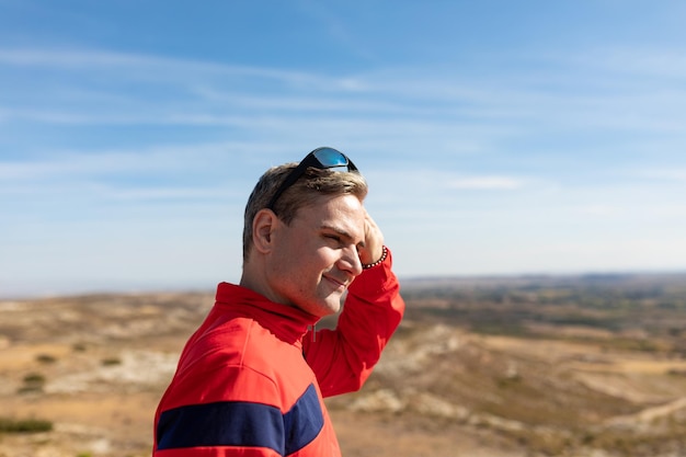 Ein Mann in einem Trainingsanzug nimmt seine Sonnenbrille ab, um von der Spitze des Hügels die Landschaft vor sich zu betrachten