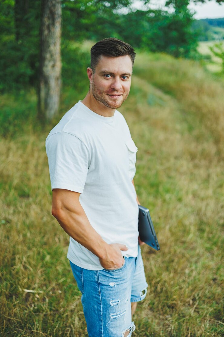 Foto ein mann in einem weißen t-shirt mit einem laptop steht in der natur und schaut in die ferne ein mann ruht in der natur von der arbeit