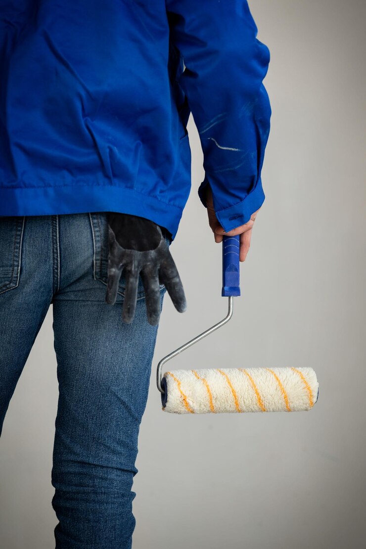 Ein Mann in einer blauen Arbeitsjacke und Jeans mit einer Farbrolle in der Hand