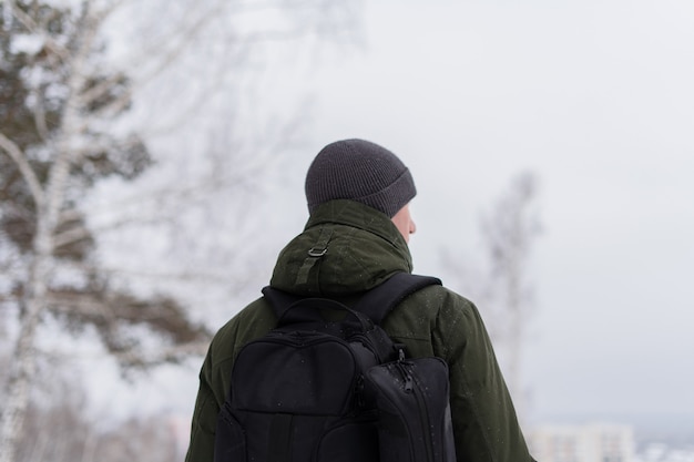 Ein Mann in einer grünen Jacke und mit einem Rucksack steht mit dem Rücken zur Kamera vor dem Hintergrund der Winterlandschaft