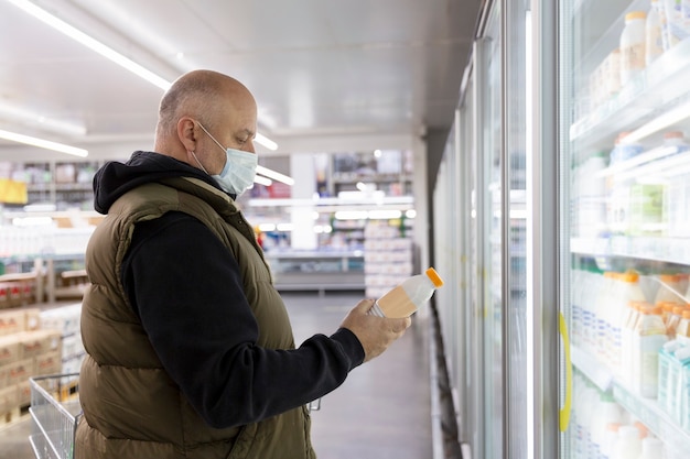 Ein Mann in einer medizinischen Maske in der Abteilung mit Milchprodukten in einem Supermarkt. Coronavirus Pandemie.