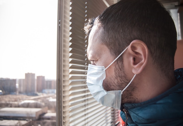 Ein Mann in einer medizinischen Maske schaut vom Balkon aus. Es ist unter Quarantäne.