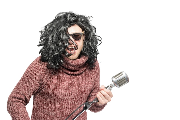Ein Mann in einer Perücke, einem Pullover und einer Sonnenbrille, die ein Mikrofon isoliert hält