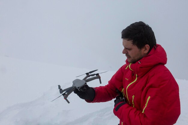 Ein Mann in einer roten Jacke hält eine Drohne vor den Schnee.