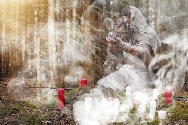 Ein Mann in einer Soutane verbringt ein Ritual in einem dunklen Wald mit einer Kristallkugel und einem Buch