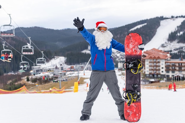 ein Mann in einer Weihnachtsmütze mit einem Snowboard in einem Skigebiet.