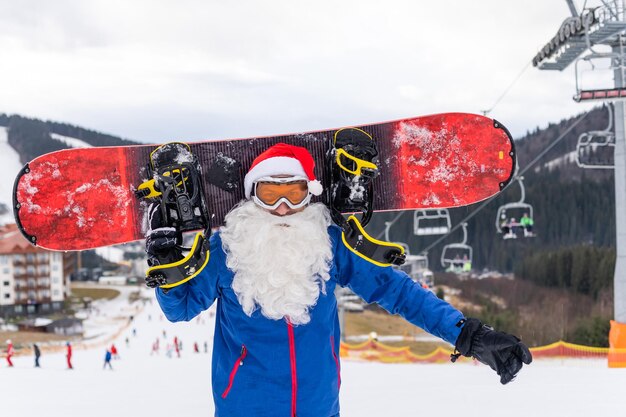 Ein mann in einer weihnachtsmütze mit einem snowboard in einem skigebiet.