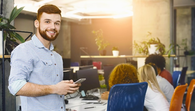 Ein Mann in formeller Kleidung steht in einem Büro und konzentriert sich auf den Bildschirm seines Handys.