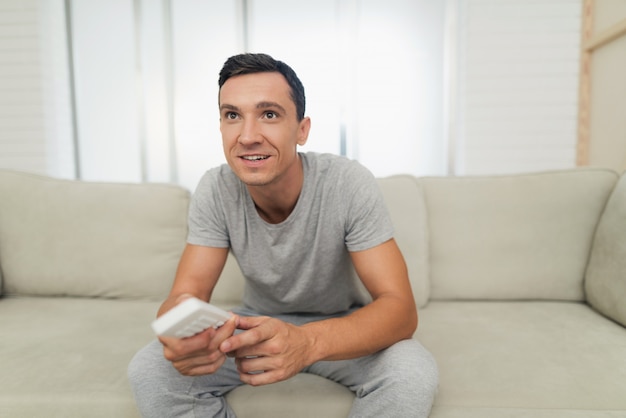 Ein Mann in grauer Hauskleidung sitzt auf dem Sofa und ruht sich aus.