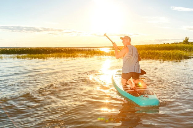 Ein Mann in kurzen Hosen sitzt bei Sonnenuntergang auf einem Sup-Board im Wasser