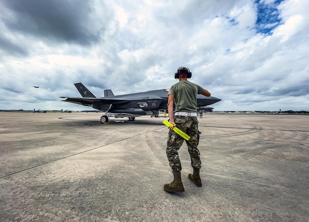 Ein Mann in Militäruniform steht auf dem Rollfeld, im Hintergrund ein Jet.