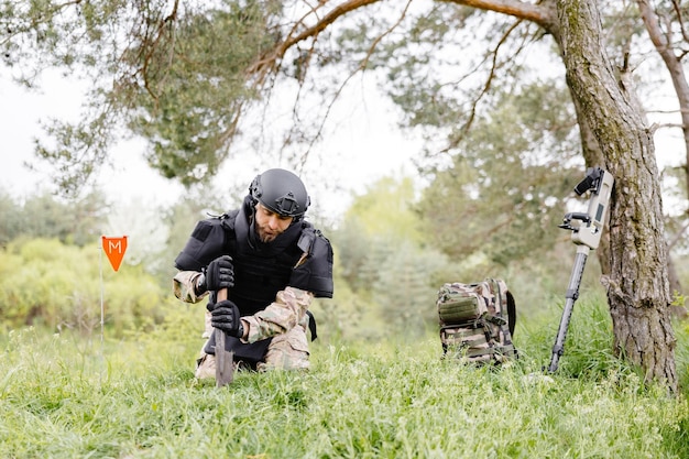 Ein Mann in Militäruniform und kugelsicherer Weste arbeitet im Wald an der Minenräumung des Territoriums