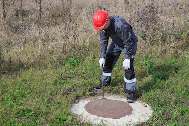 Ein Mann in Overall und Helm öffnet einen Wasserbrunnen mit einem Brecheisen Inspektion und Reparatur von Wasserbrunnen und Zählern