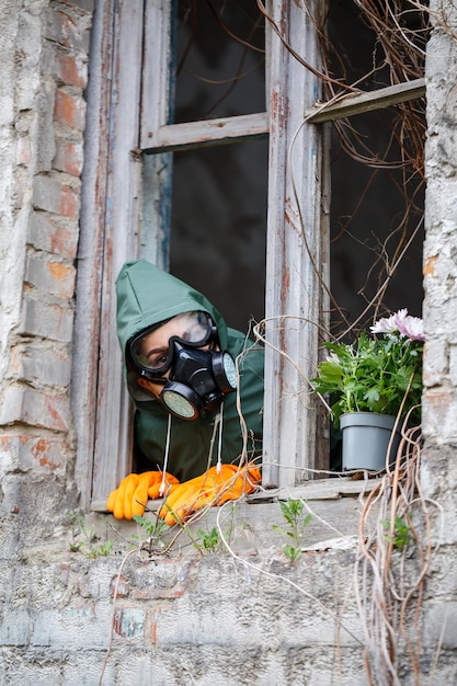 Ein Mann in Regenmantel und Gasmaske sammelt eine Blume aus einer verbrannten giftigen Erde Luftverschmutzungskonzept Ökologische Katastrophe