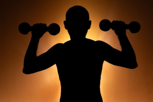 Ein Mann in Silhouette macht eine körperliche Übung mit zwei Hanteln