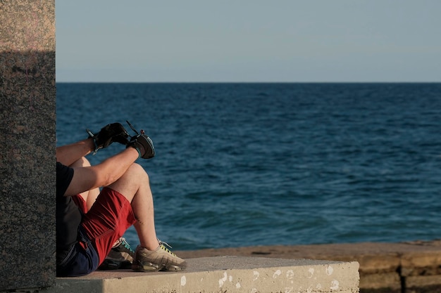 Ein Mann in Sportkleidung sitzt an einem Sommerabend auf einem Pier und blickt aufs Meer