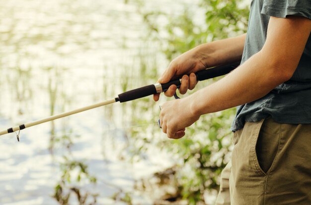 Ein Mann in T-Shirt und dunkler Hose fischt auf dem See mit einer weißen Angelrute gegen Büsche und Gras