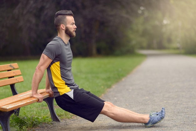 Ein Mann in voller Länge, der auf einer Bank im Park Push-ups macht