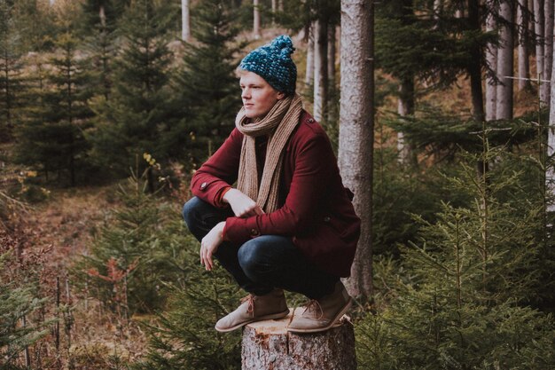 Foto ein mann in voller länge, der im winter auf einem baumstumpf im wald hockt