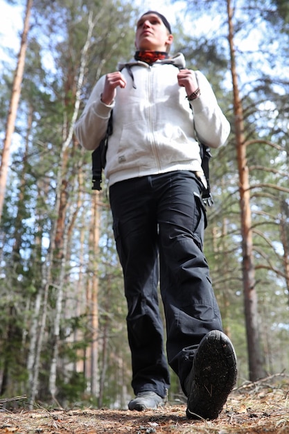 Ein Mann ist ein Tourist in einem Kiefernwald mit einem Rucksack. Eine Wanderung durch den Wald. Kiefernreservat für touristische Spaziergänge. Ein junger Mann bei einer Wanderung im Frühjahr.