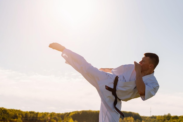 Ein Mann Karate-Kämpfer im weißen Kimono-Training im Freien im Park
