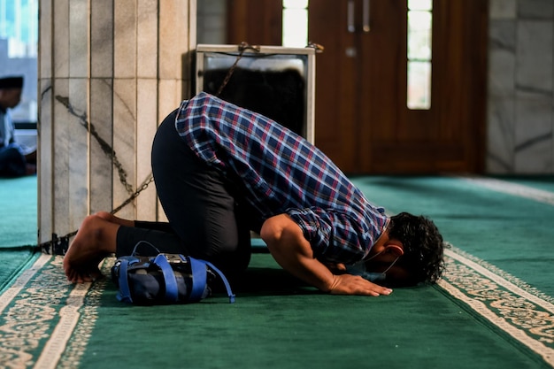 Ein Mann kniet auf einem Teppich in einer Moschee, mit einer blauen Tasche auf dem Kopf in Tangerang City, Indonesien