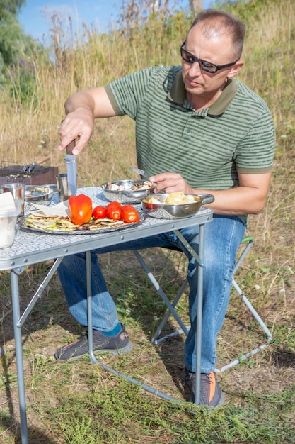 Ein Mann kocht an einem Lagerfeuer im Gras.