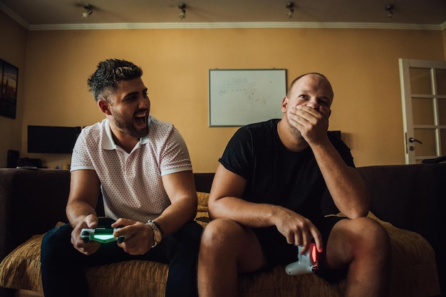 Ein Mann lacht über einen enttäuschten Freund, während er zu Hause ein Videospiel spielt