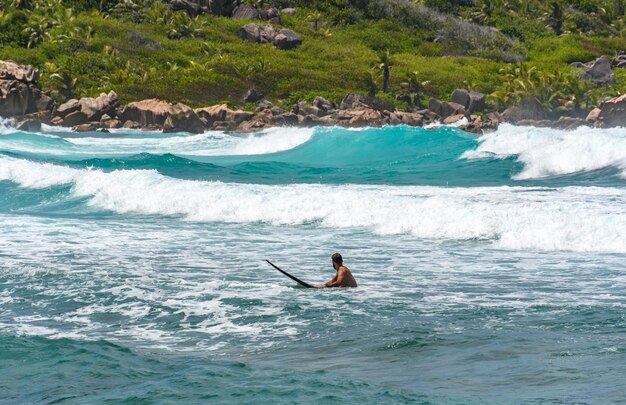 Foto ein mann liegt auf einem surfbrett auf wellen auf einem türkisfarbenen ozean in einer idyllischen tropischen bucht