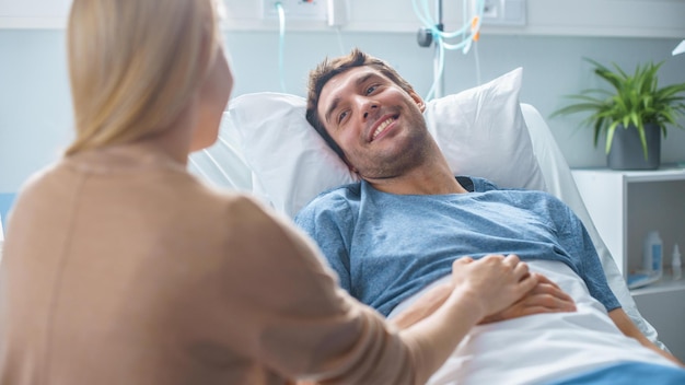 Ein Mann liegt in einem Krankenhausbett und sieht seine Frau an.
