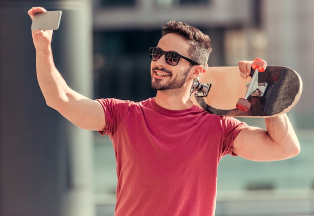 Ein Mann macht ein Selfie mit einem Skate in der Hand.