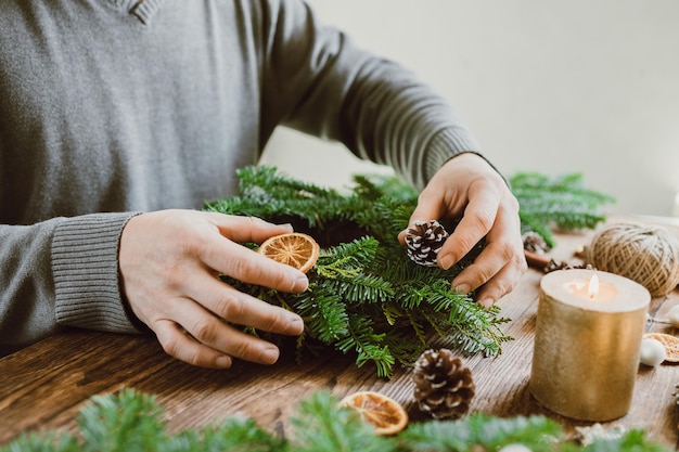 Ein Mann macht eine Weihnachtsdekoration für sein Zuhause aus frischen Fichtenzweigen und getrockneten Orangenstücken