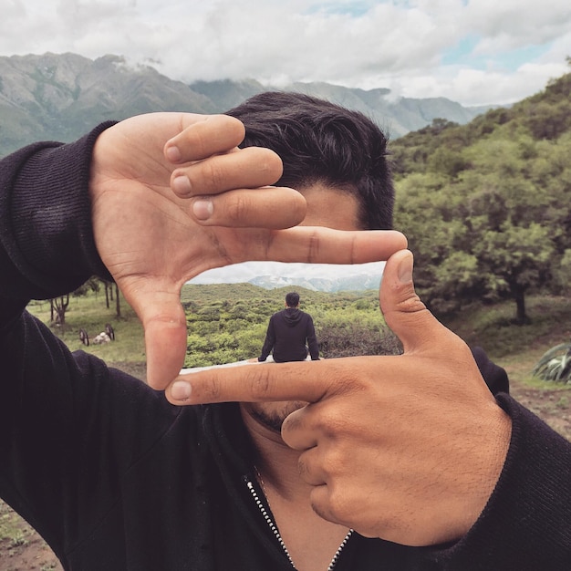 Foto ein mann macht einen rahmen mit einer person, die gegen die landschaft sitzt