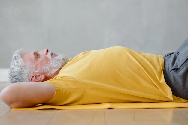 Ein Mann macht Yoga und Fitness im Fitnessstudio auf einer gelben Matte Senior Yoga zu Hause oder im