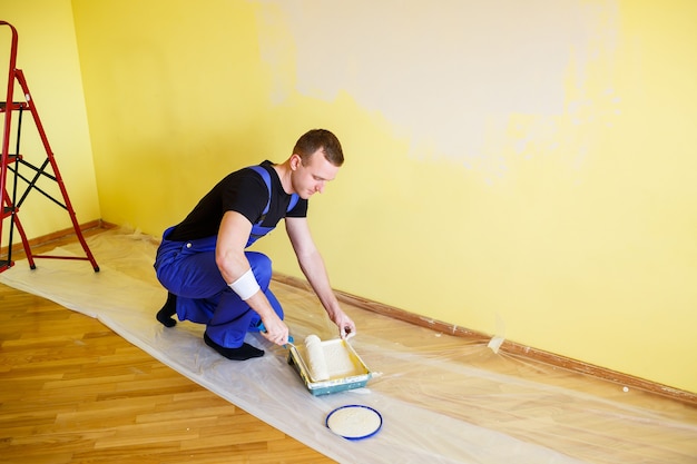 Ein Mann malt die Wand im Haus mit Rolle und Farbe. Renovierung der Zimmer im Haus.